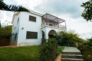 A two-story white house with a balcony, a stone staircase, and a well-maintained garden. - Kalina Complex (Pomos)