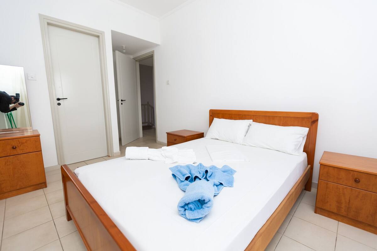 A neatly made bed with white and blue towels, wooden headboard, and two wooden nightstands.