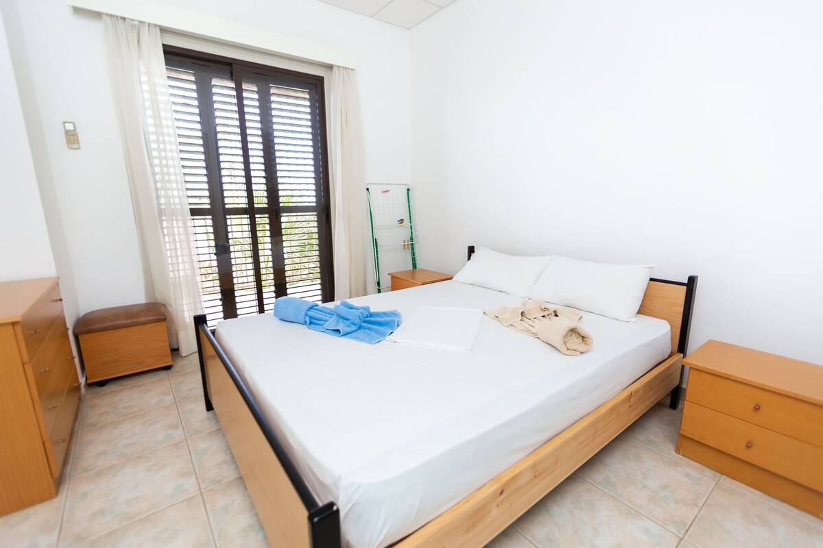 A neatly arranged bedroom with a bed, bedside tables, a bench, and a window with blinds.
