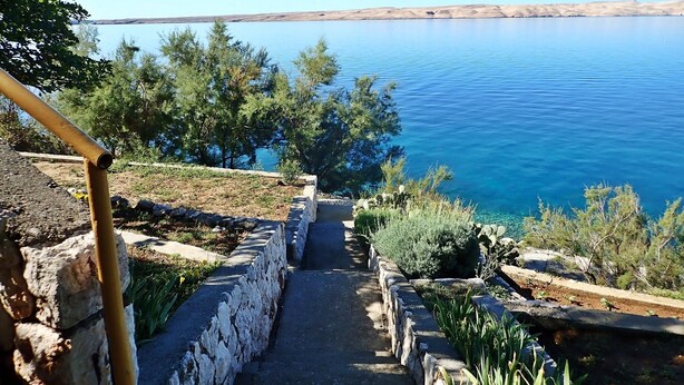Un sentier de pierres menant à un plan d’eau, entouré de verdure et sous un ciel dégagé.