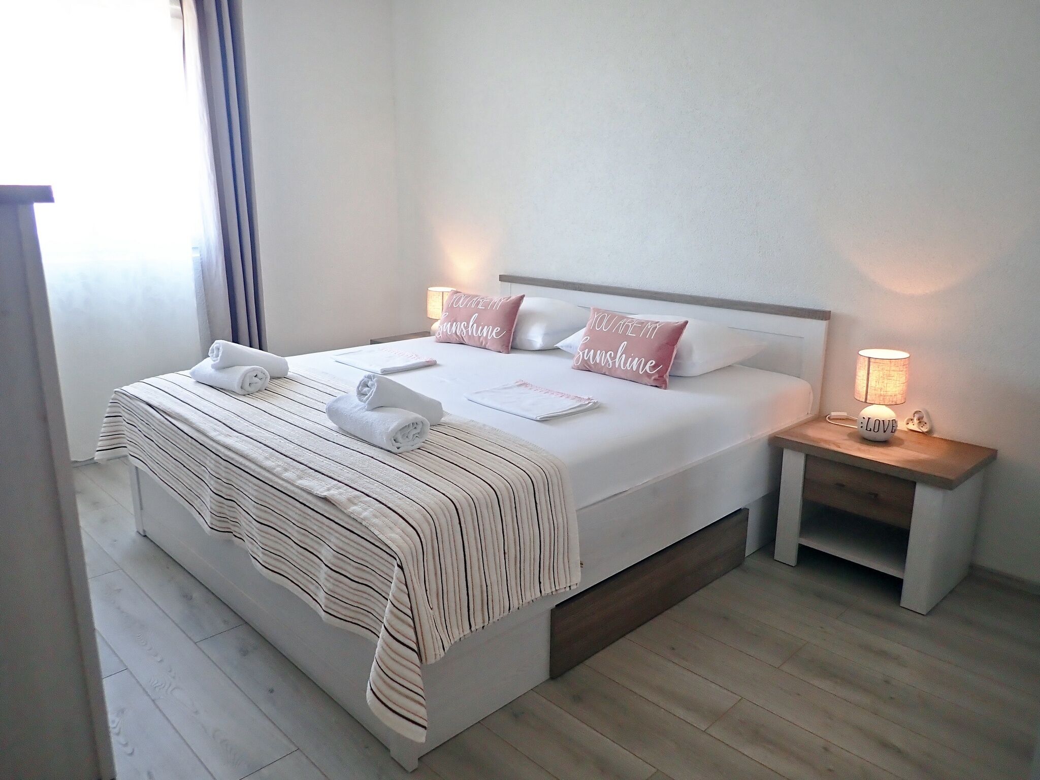 A neatly made bed with striped bedding, two pillows with text, a bedside lamp, and a nightstand.