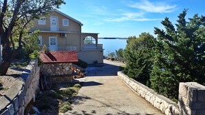 Une maison située sur la côte, dotée d’un mur en pierre, d’un espace barbecue avec un toit rouge et offrant une vue sur la mer.