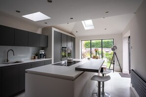 A modern kitchen with a central island, dark cabinets, and a large window offering a view of the outdoors. - Contemporary Bright House 20 Min To Manc (Stockport)