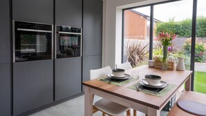 A modern kitchen with built-in ovens and a dining area with a table set for two. - Contemporary Bright House 20 Min To Manc (Stockport)