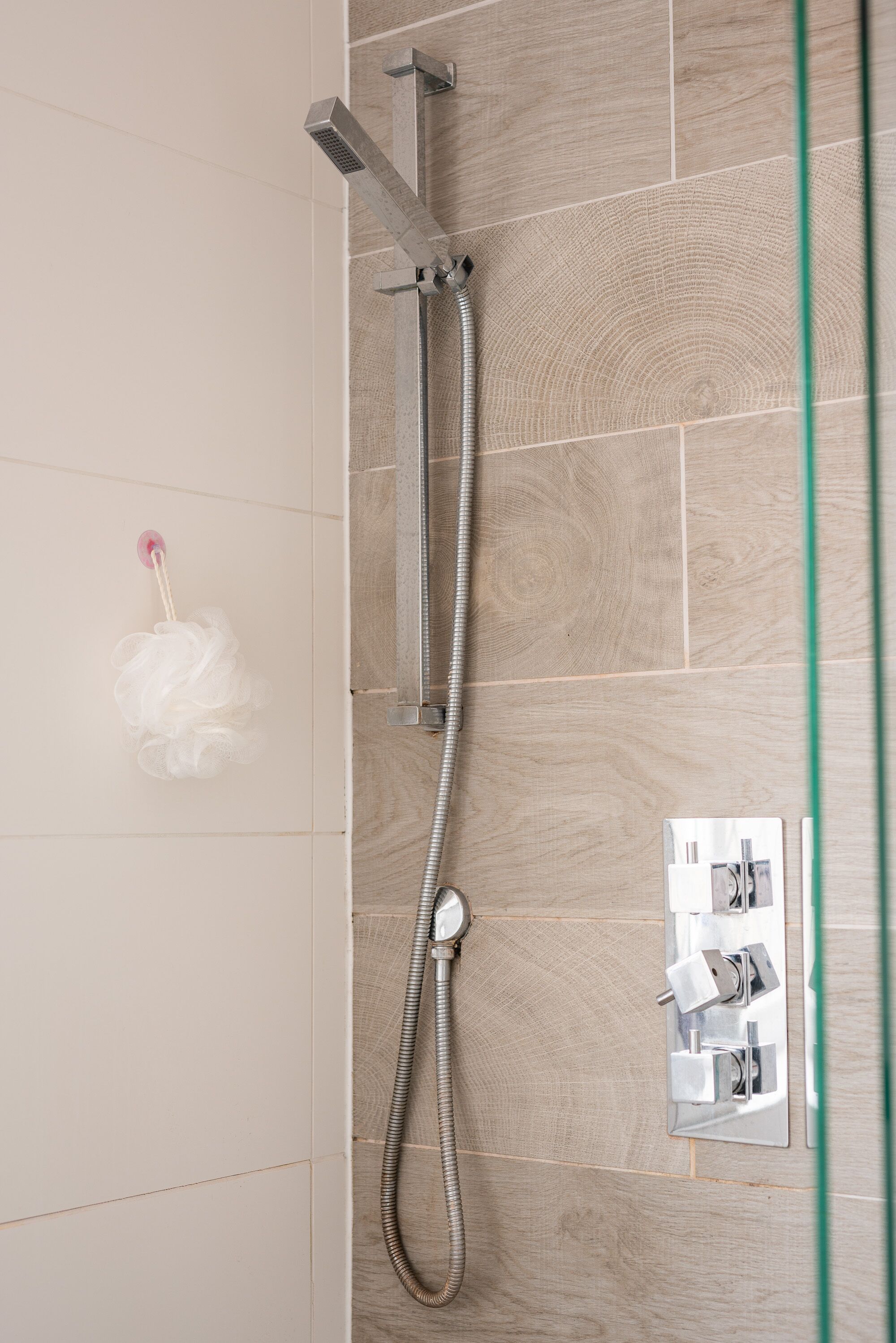 A shower with a handheld showerhead and a wall-mounted control panel.