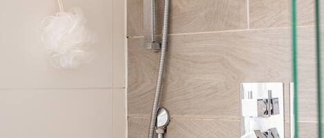 A shower with a handheld showerhead and a wall-mounted control panel.