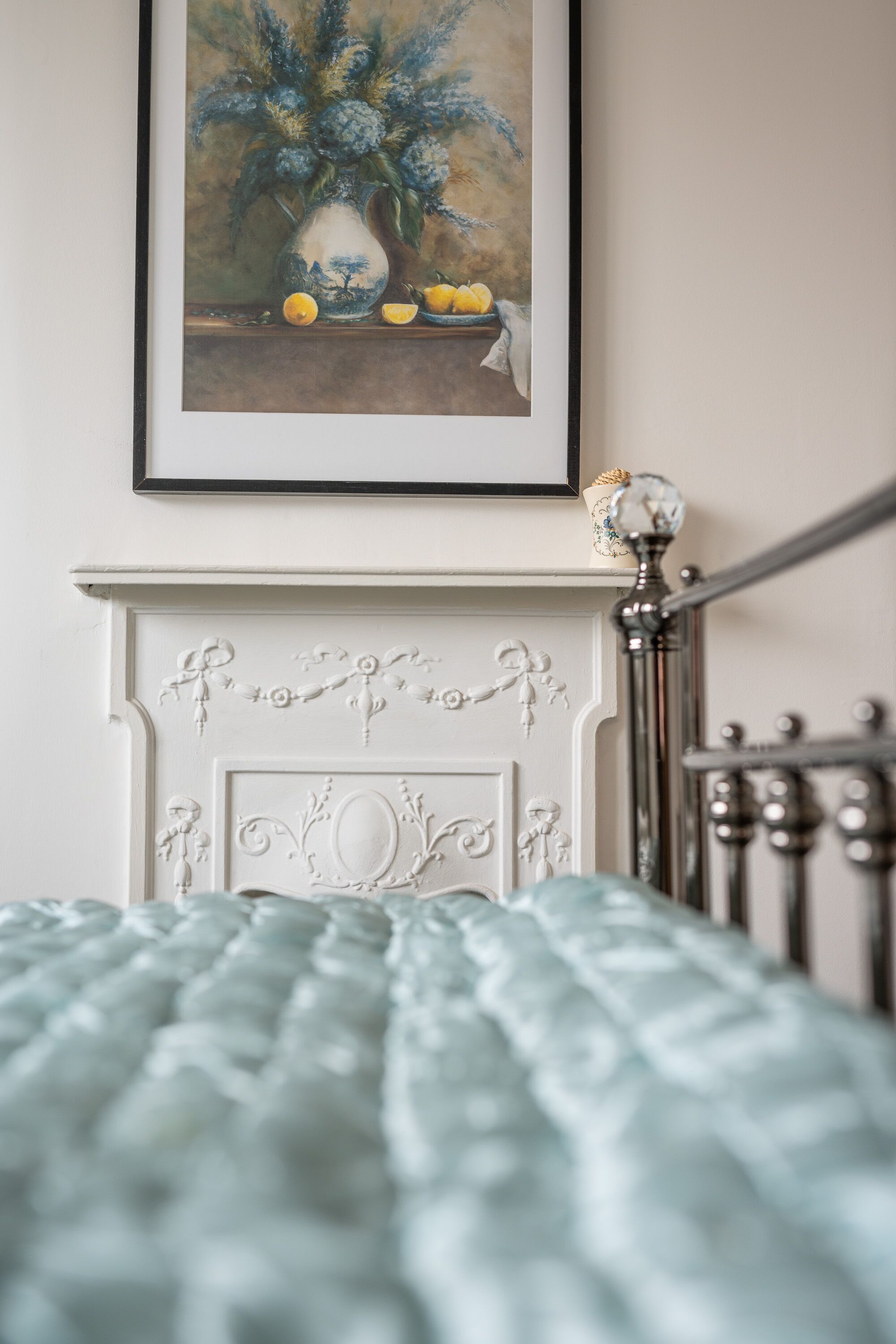 A bedroom with a bed, a fireplace, and a framed painting above it.