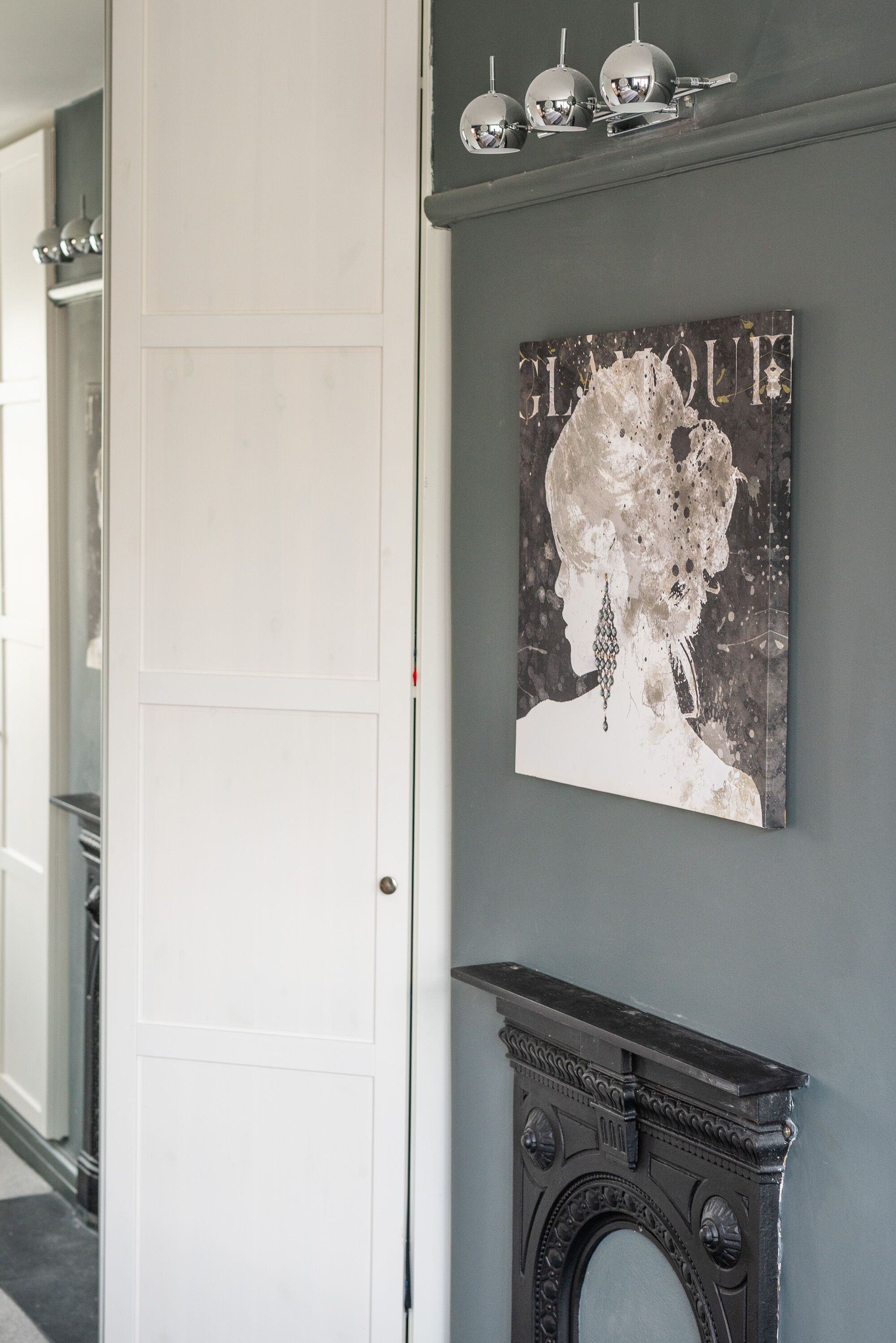 A hallway with a white door, a fireplace with a decorative mantel, and a wall-mounted artwork depicting a figure with the word "GLAMOUR" above it.