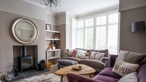 A cozy living room with a fireplace, a sofa, a coffee table, and a large window with blinds. - Contemporary Bright House 20 Min To Manc (Stockport)