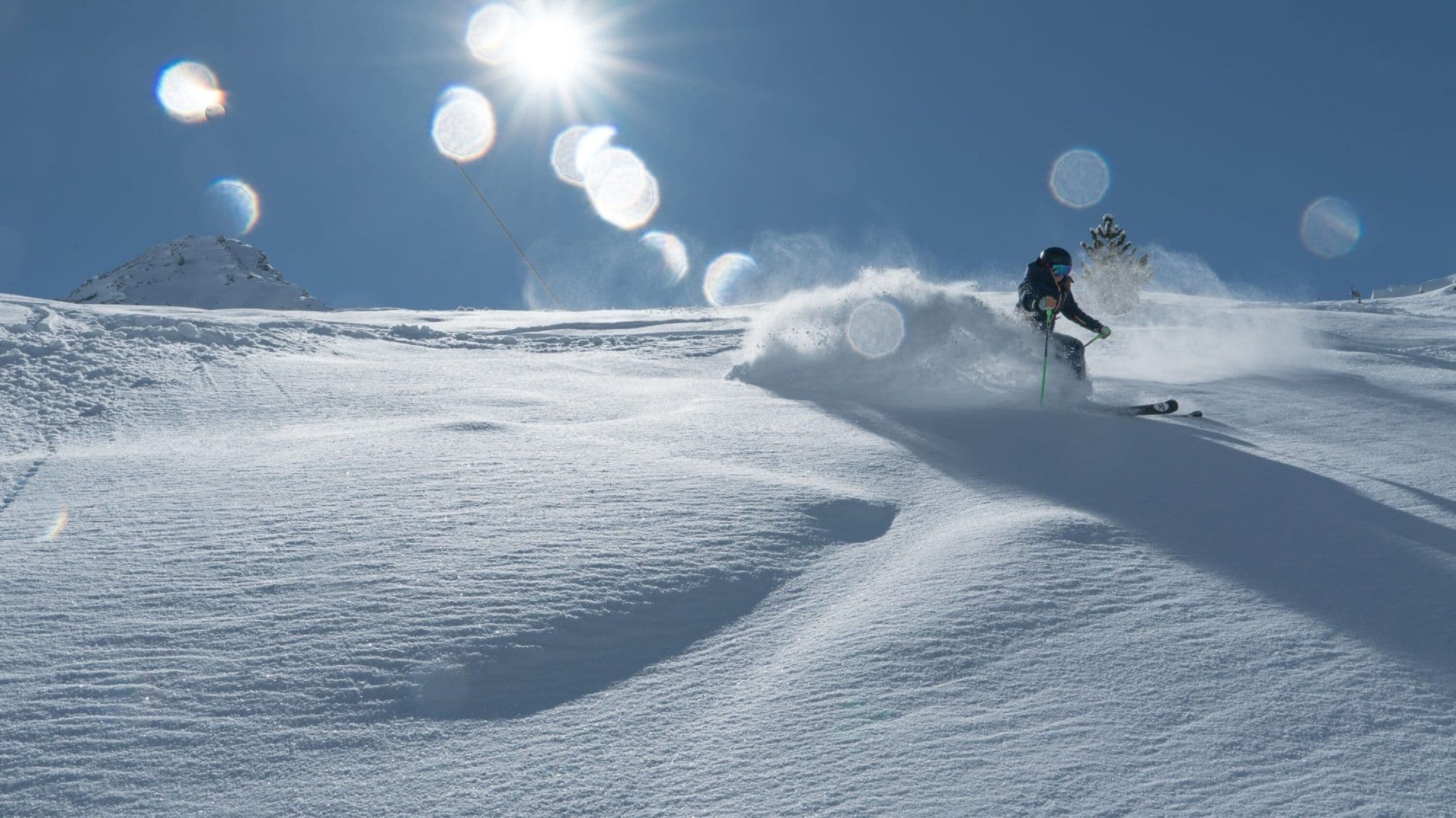 A snowy landscape with a skier in motion, creating a spray of snow.