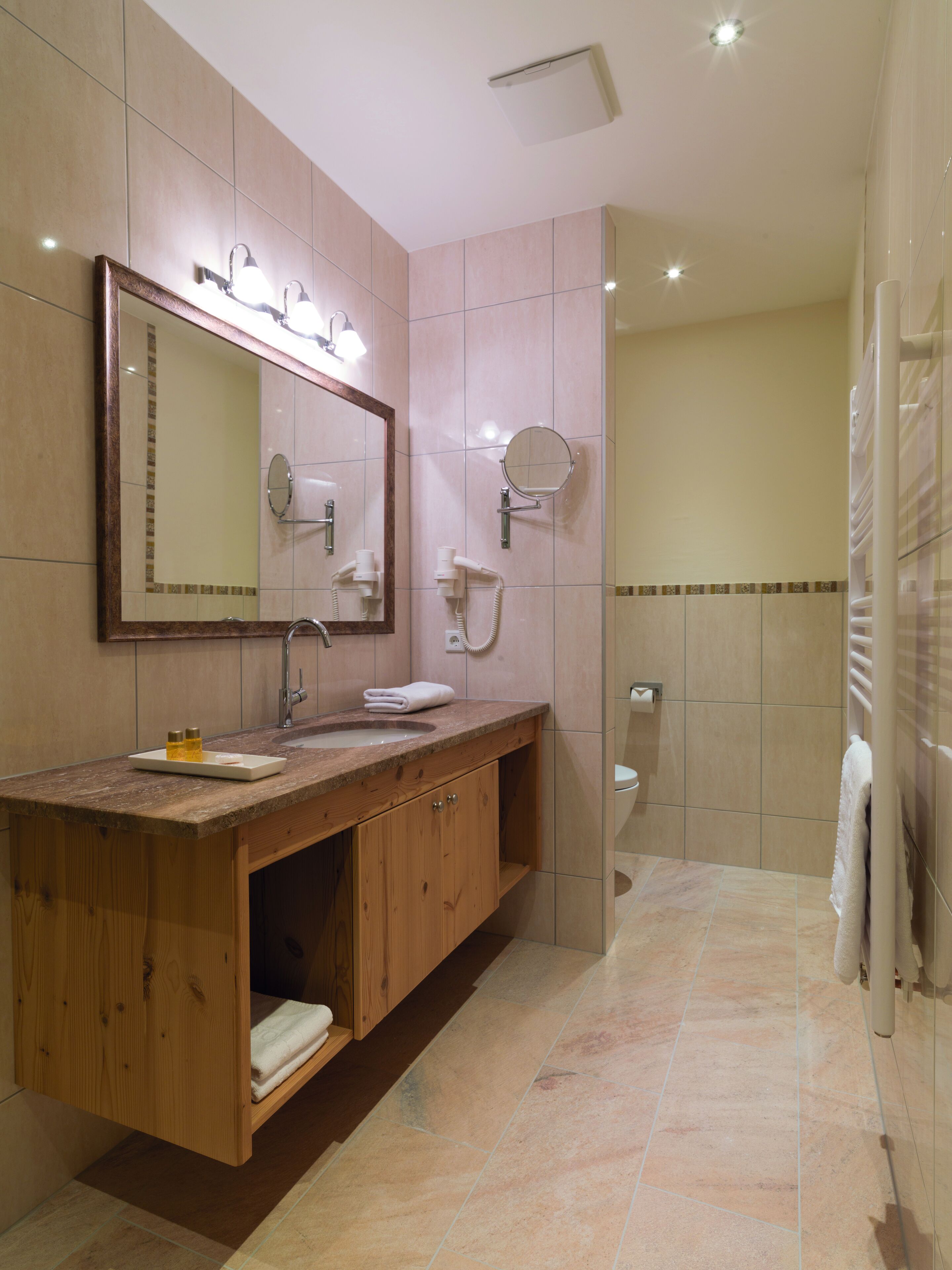 A bathroom with a wooden vanity, a large mirror, a sink, a towel rack, and a shower area.