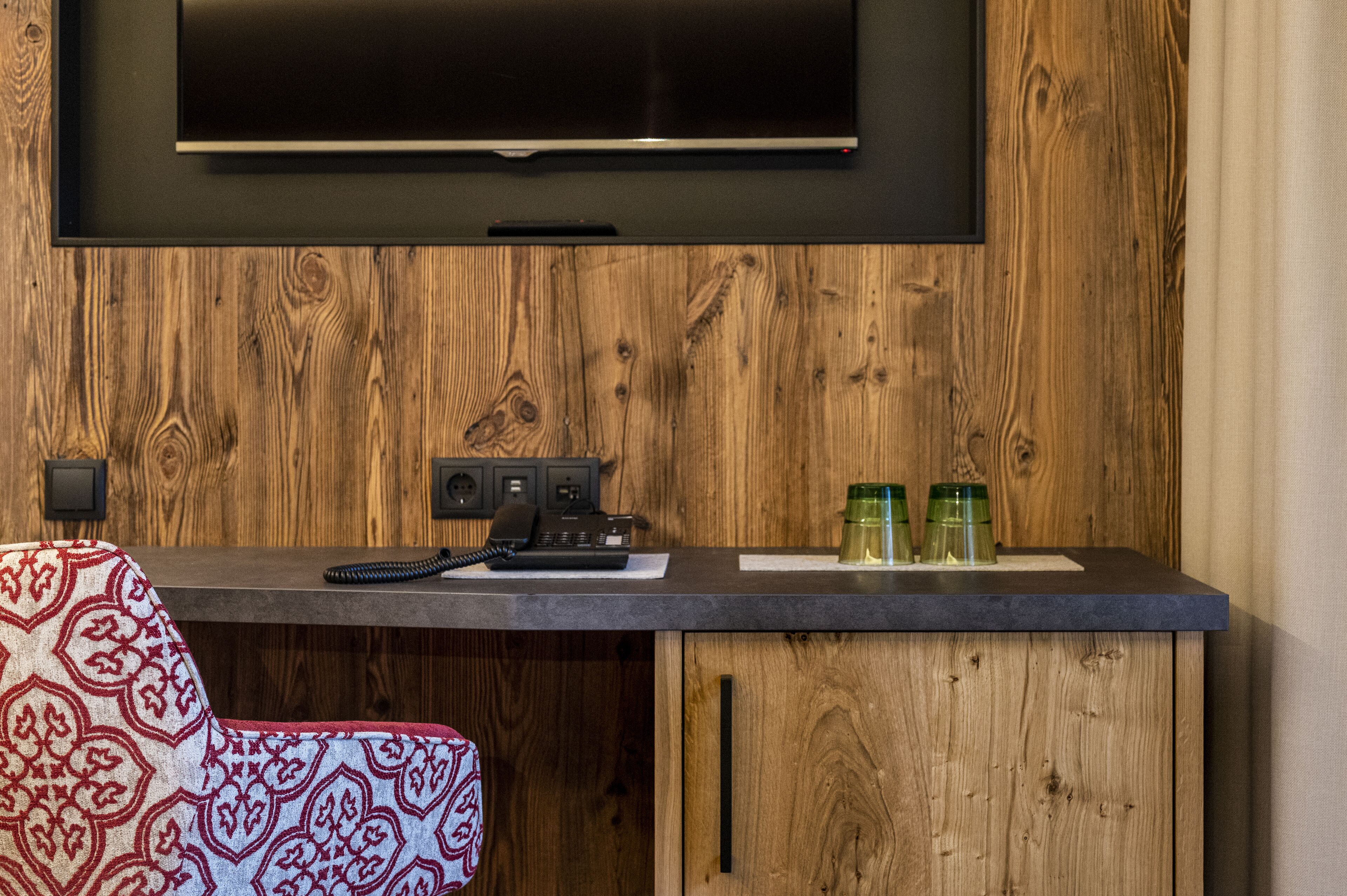 Una habitación con pared de madera, un televisor de pantalla plana montado sobre un mostrador, un teléfono y dos botellas verdes sobre el mostrador.