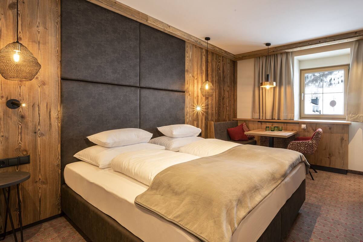 A hotel room with a large bed, a desk, a chair, and a window with curtains.