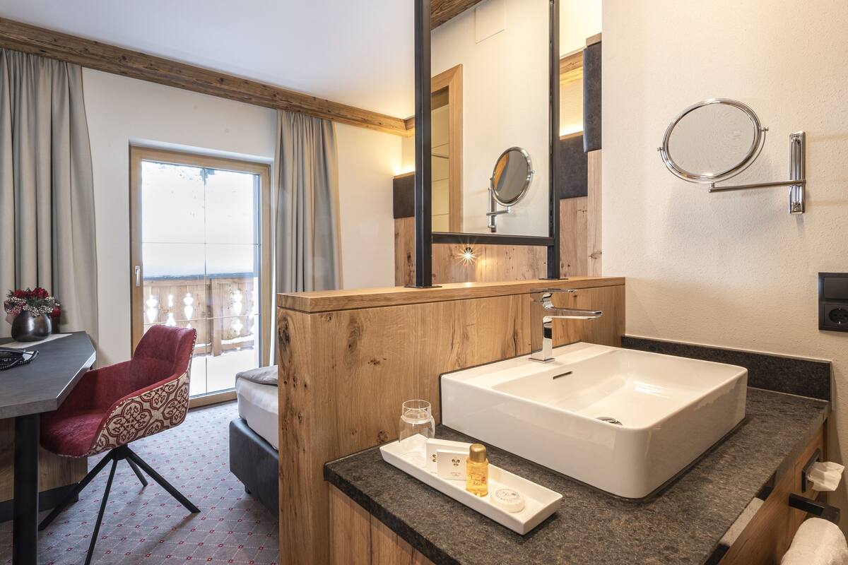 A modern hotel bathroom with a large sink, a mirror, and a wooden vanity.