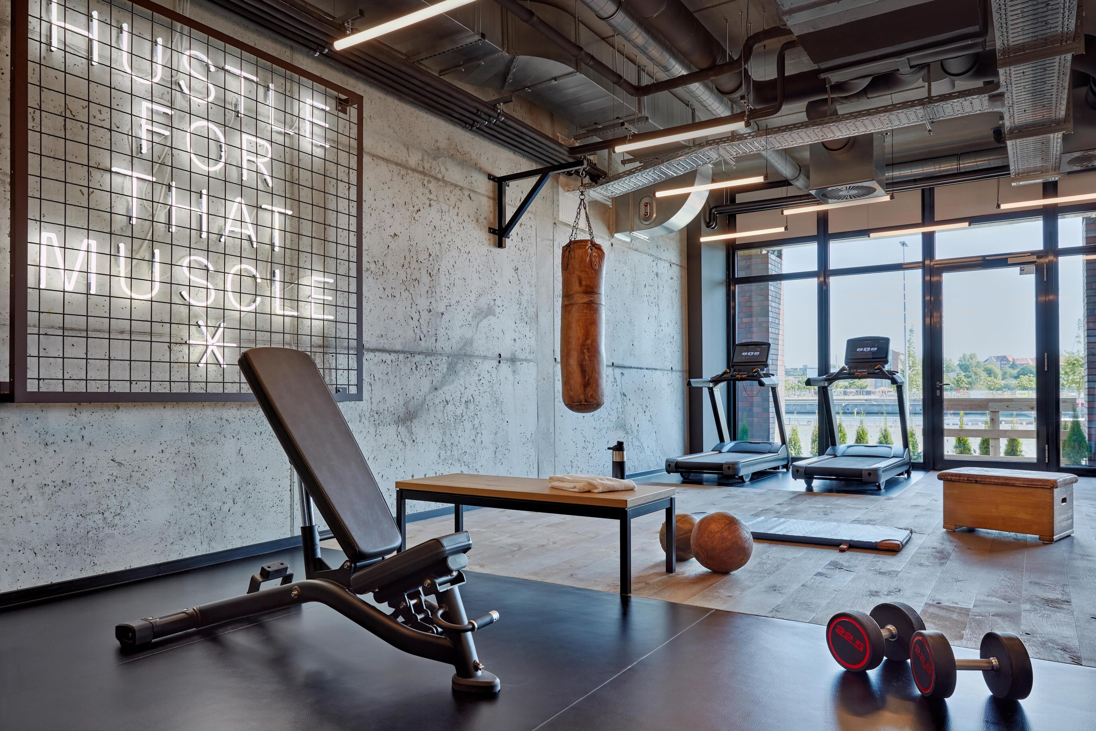 Un gimnasio con saco de boxeo, banco de pesas, mancuernas, cintas de correr y prensa de pesas.