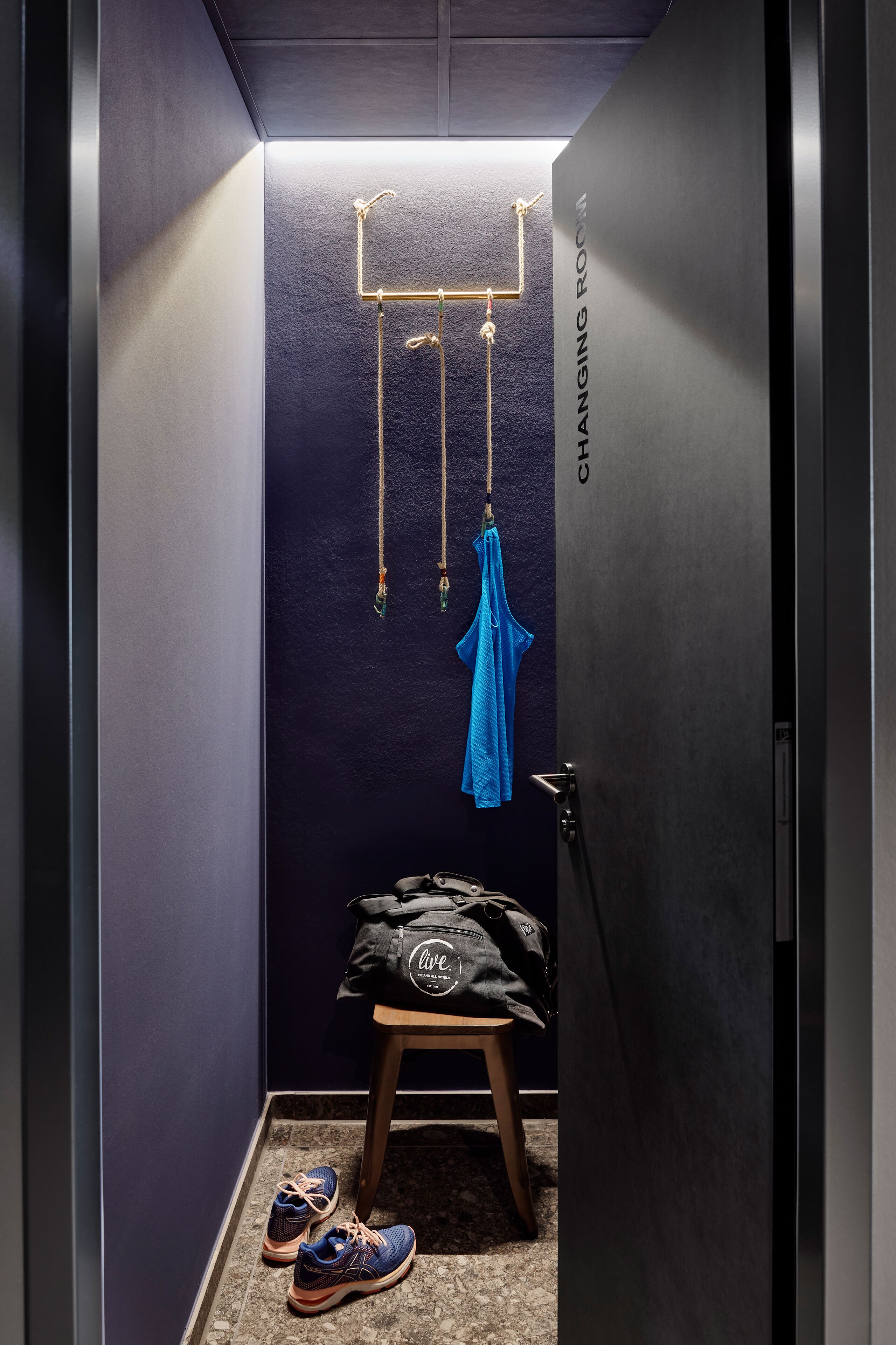 Una habitación pequeña con una pared azul oscuro, un sillón colgante, un taburete y un par de zapatos en el suelo.
