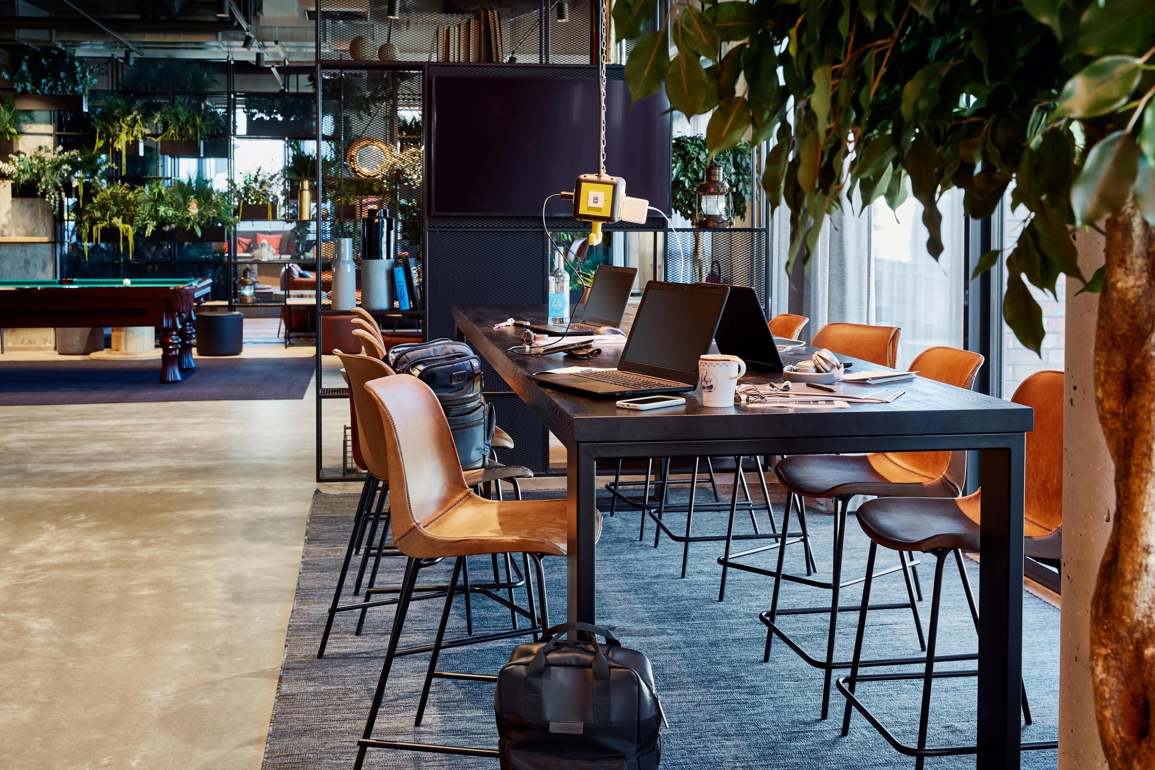 A modern office space with a long table, multiple chairs, laptops, and a pool table.