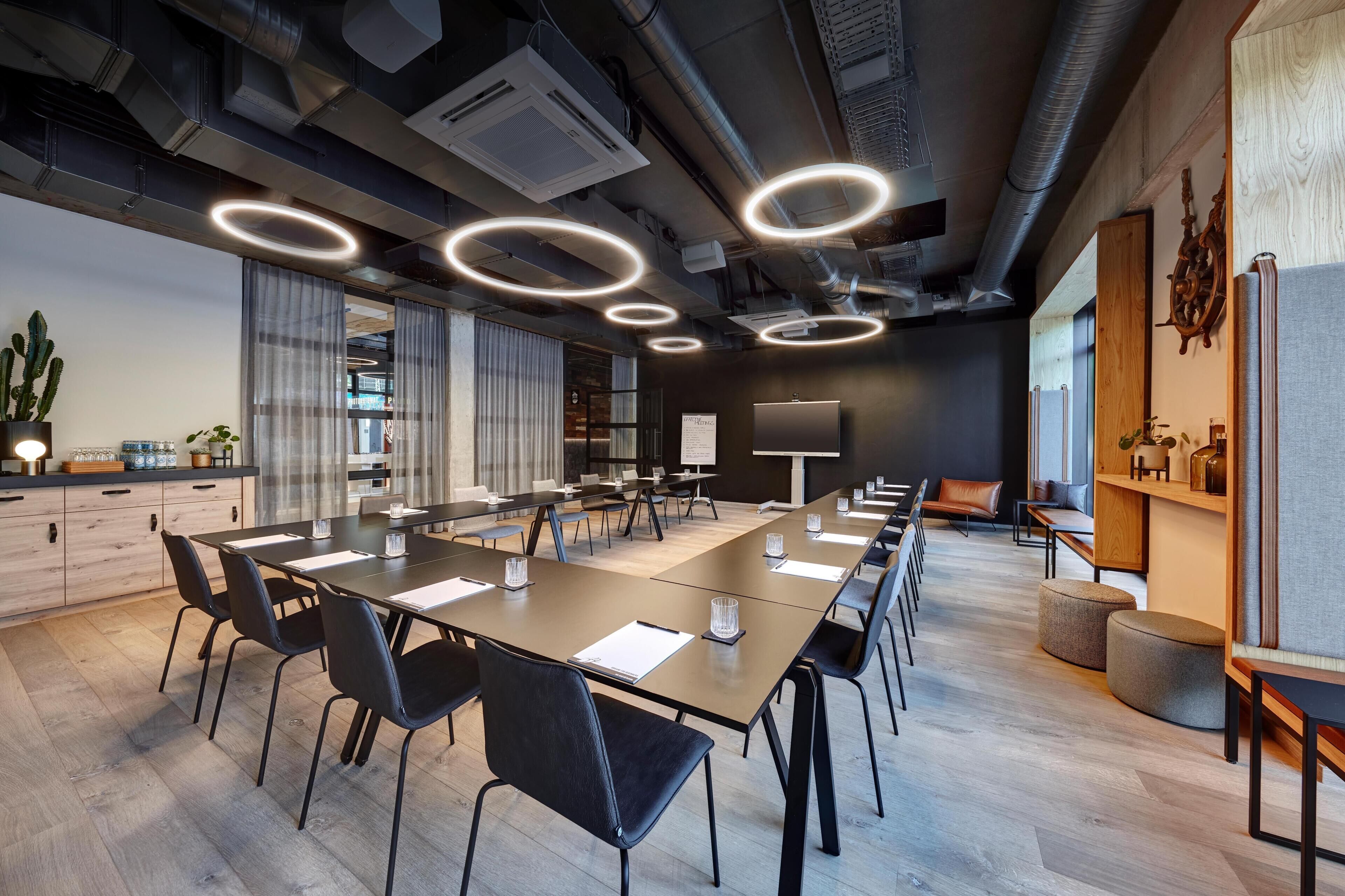 A modern conference room with a long table, black chairs, and circular ceiling lights.