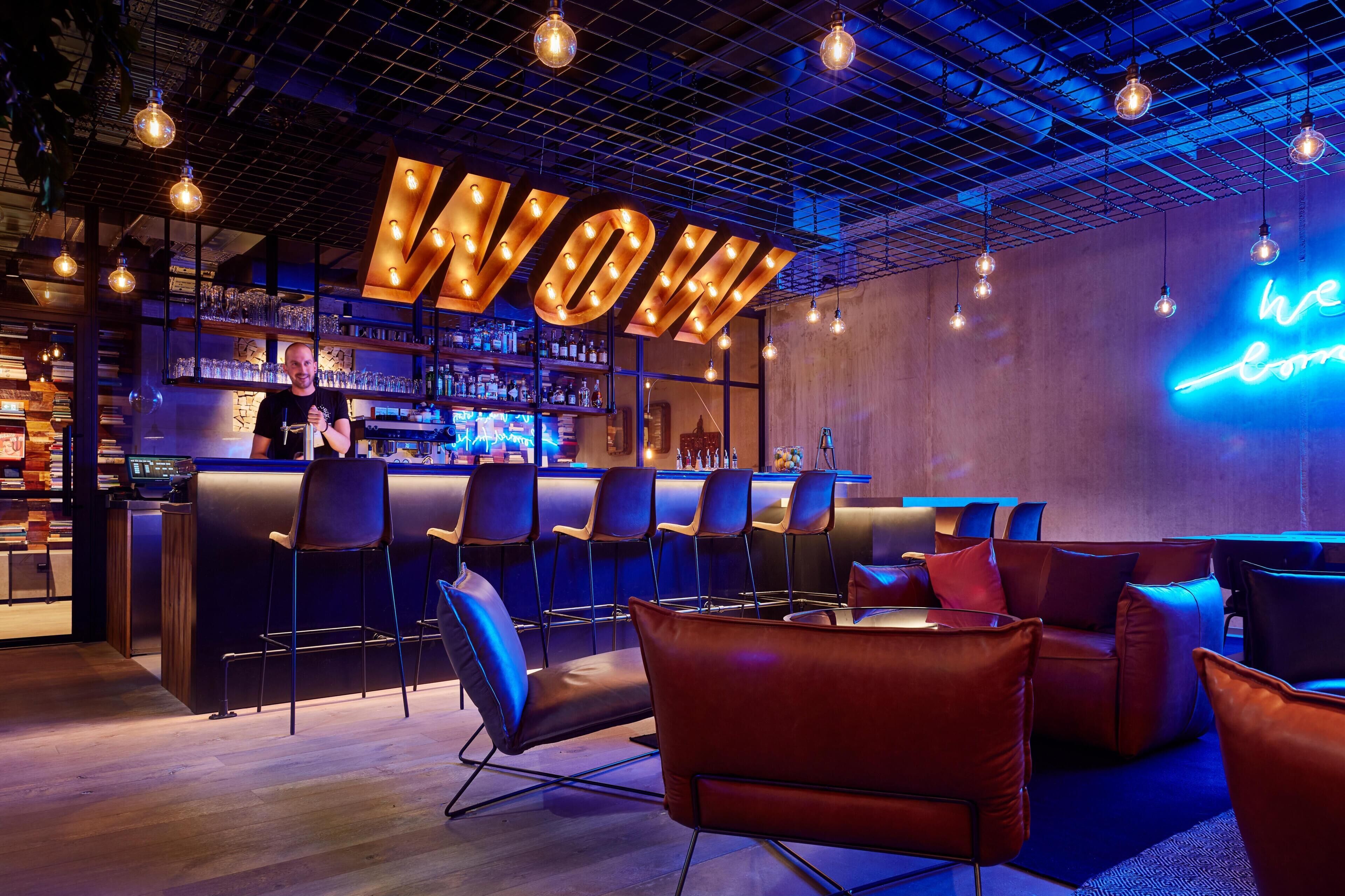Uma área de bar com um letreiro de neon que diz 'WOW' e outro letreiro de neon que diz 'nós viemos de'.