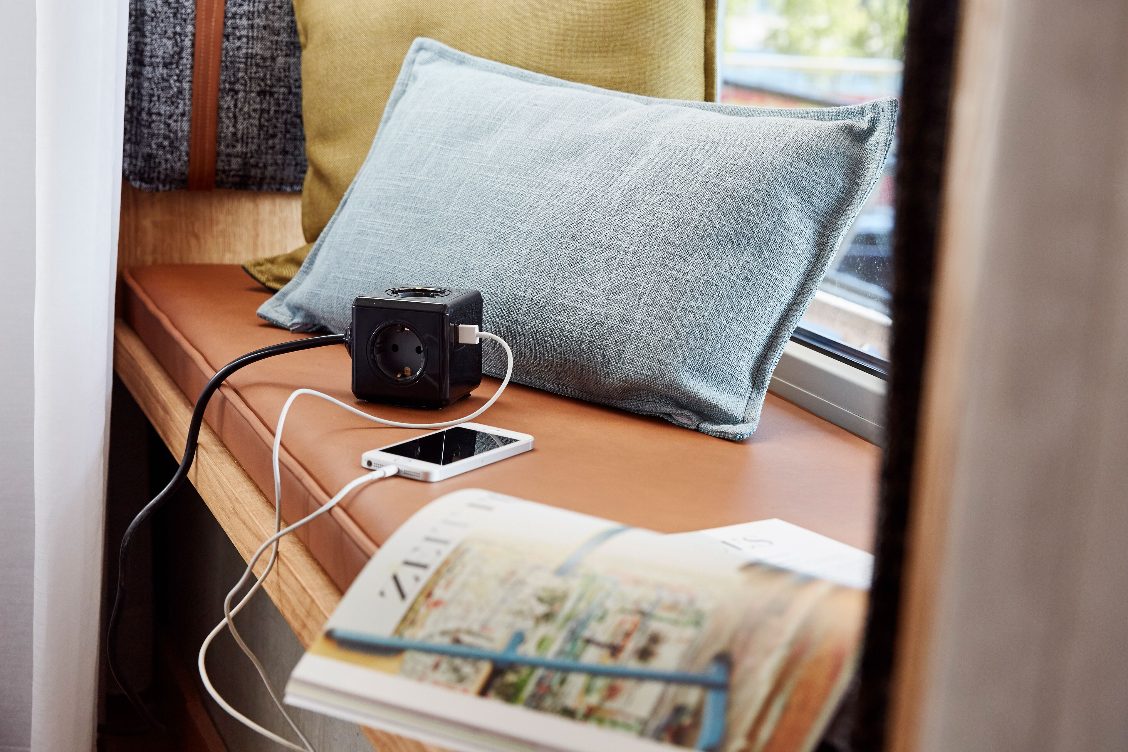 A bed with a pillow, a camera, a smartphone, and a magazine on a wooden surface.