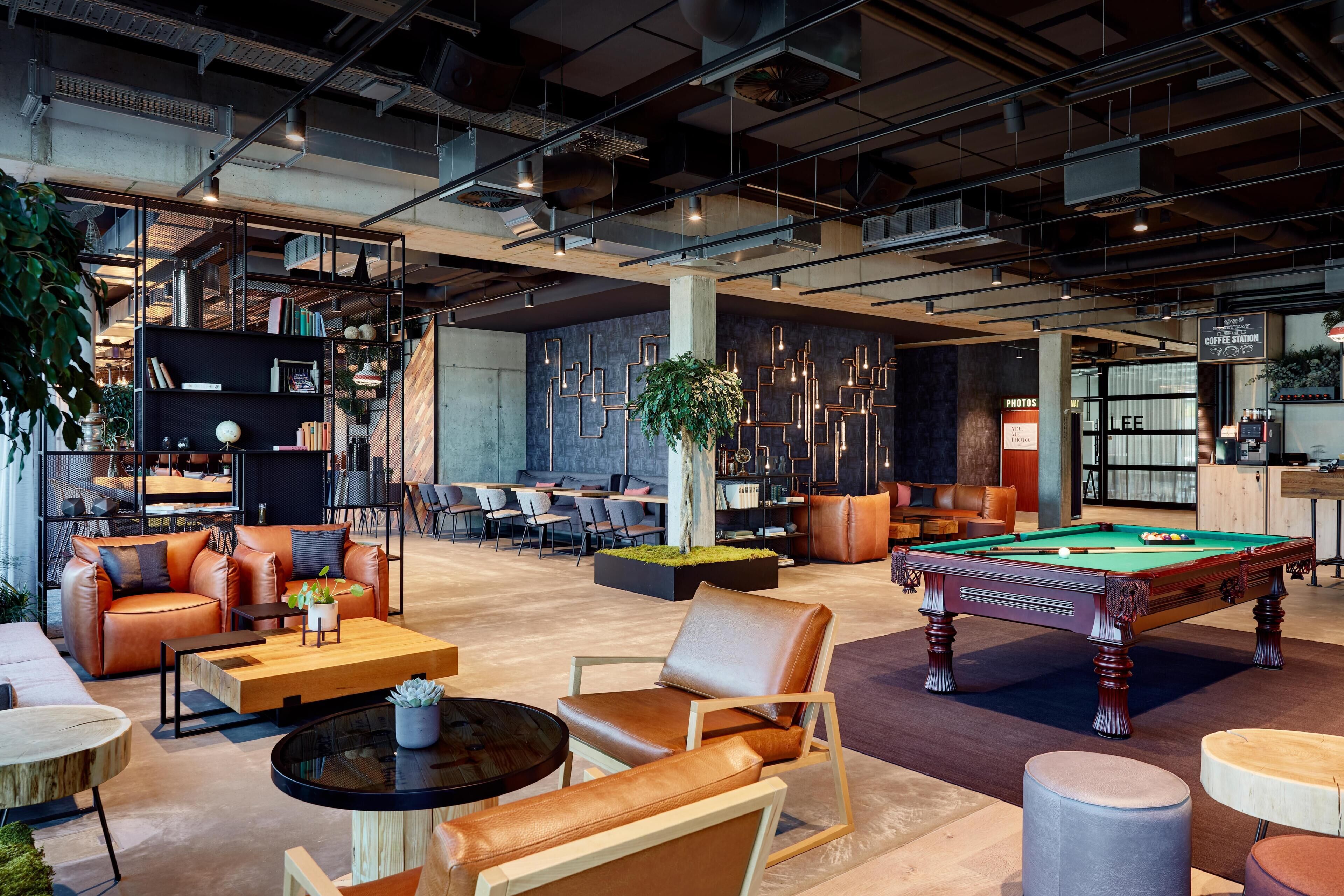 A modern lounge area with leather sofas, a pool table, and a coffee station.