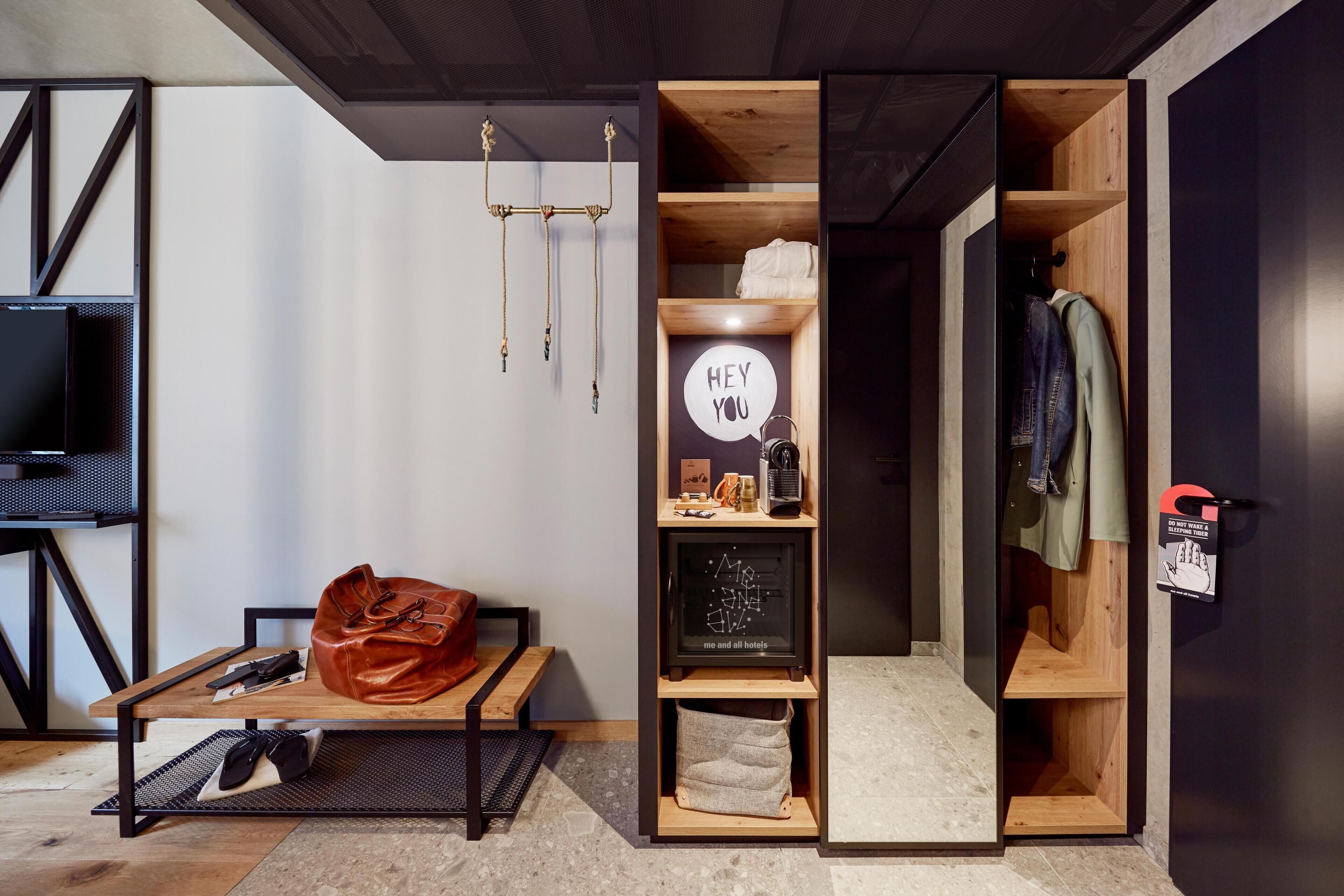 A modern hotel room with a bed, a desk, a wardrobe, and a television.