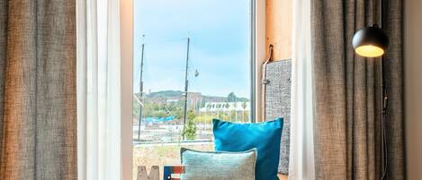 A hotel room with a large window, a bed, a nightstand, a lamp, and a view of the outside.