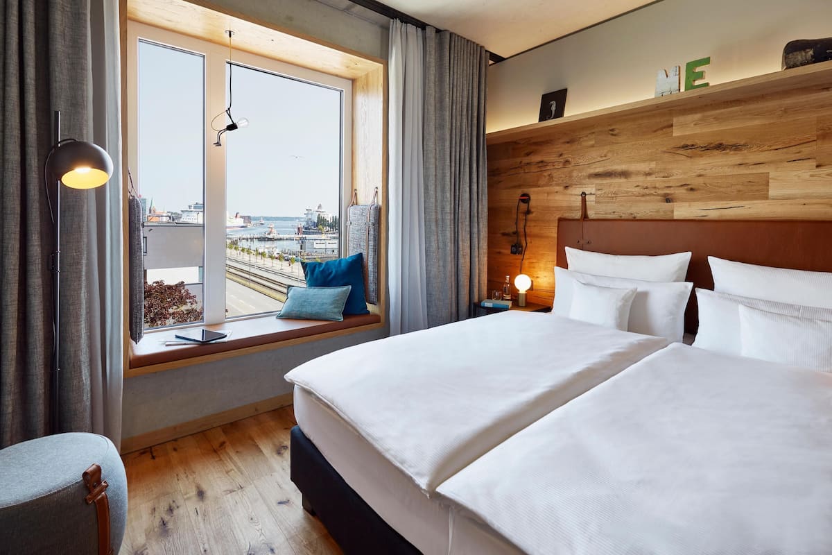 Une chambre d’hôtel avec un grand lit, un coin fenêtre offrant une vue agréable, une table de chevet avec une lampe et un panneau mural en bois.