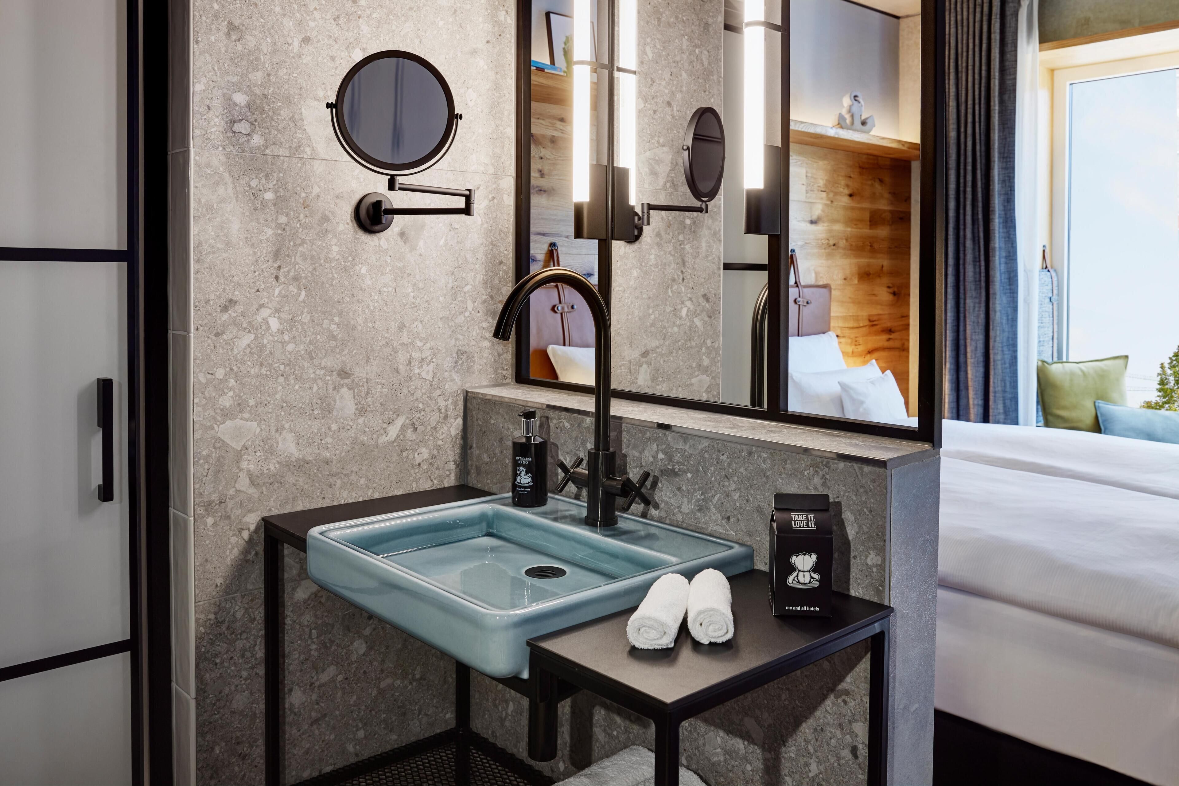 Een moderne badkamer met een rechthoekig wastafelmeubel, een ronde spiegel en een nachtkastje met een handdoek en een klein object.