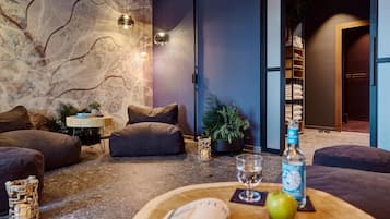 Una sala de estar moderna con una pared de piedra, un conjunto de sofás, una mesita baja con una botella y un vaso, y una planta.