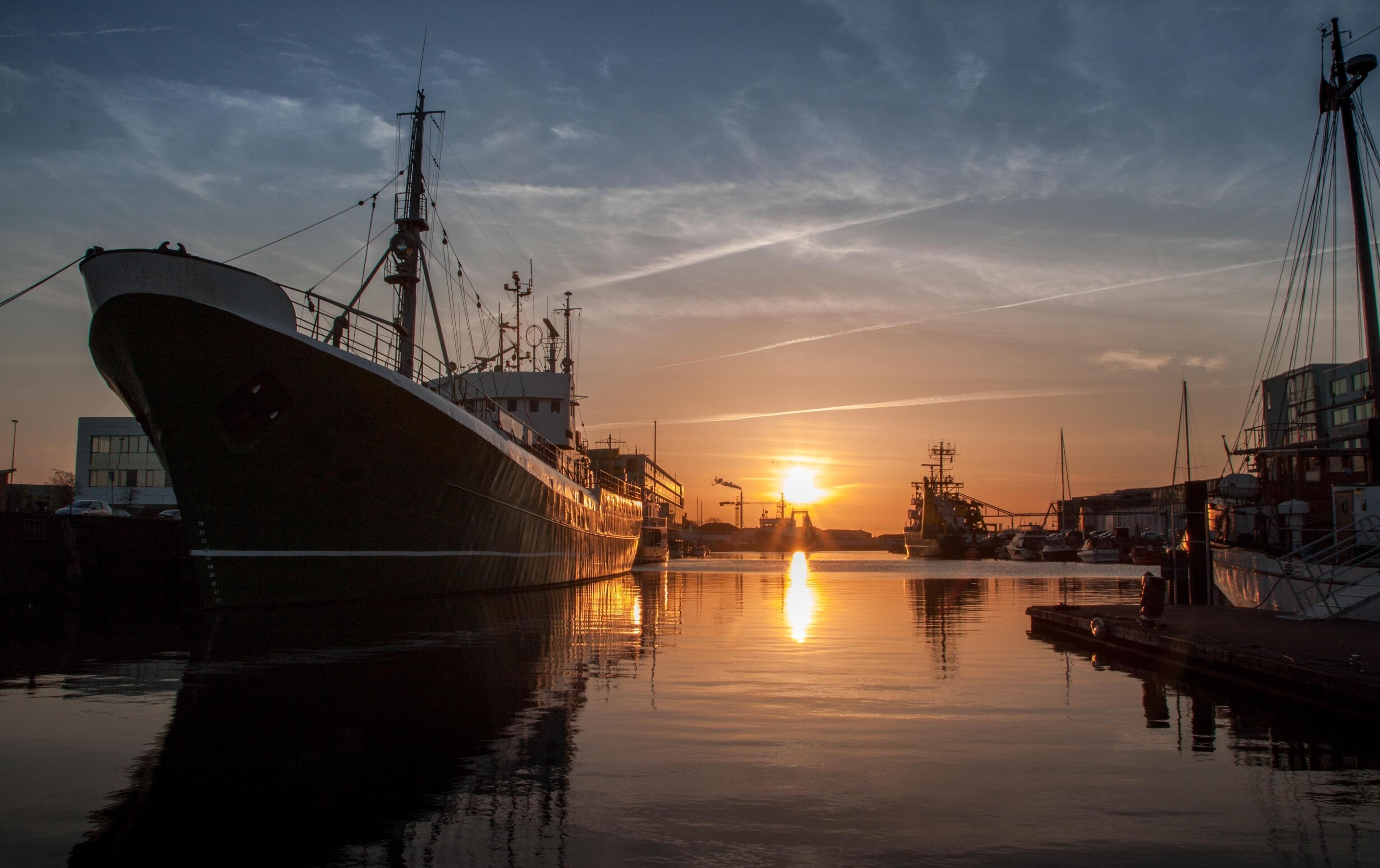 Un barco grande amarrado en un puerto, con un atardecer de fondo.