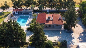 Une maison avec une piscine, une terrasse en pierre et un toit recouvert de tuiles rouges.