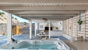 Un espace bien-être comprenant un jacuzzi, une terrasse en bois, un mur en pierre et une vue sur le paysage environnant.