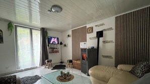 Olohuoneessa on lasinen sohvapöytä, sohva, televisio ja jääkaappi.