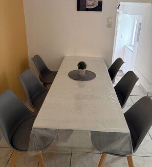 Une table à manger recouverte d’une housse en plastique transparent, entourée de six chaises.
