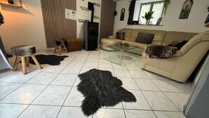 Moderni olohuone, jossa on beige sohva, lasinen sohvapöytä, musta, pörröinen matto, puinen jakkara ja pieni puinen arkku.
