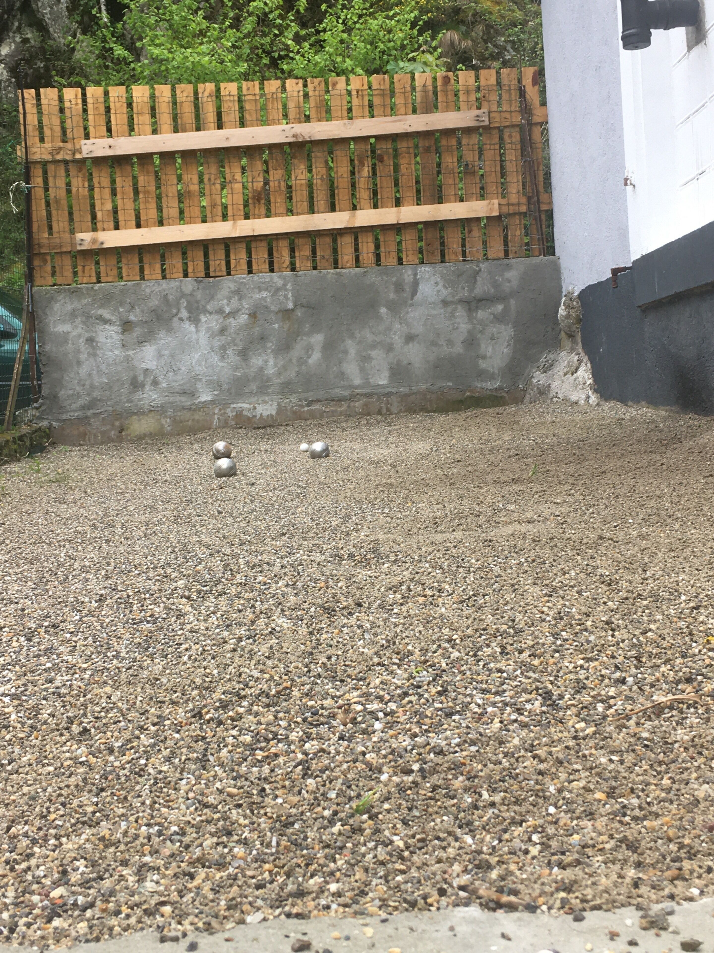 A gravel area with a wooden fence and a concrete wall.
