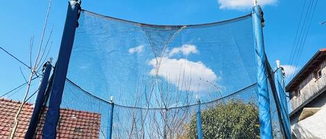Un trampoline doté d’un filet de protection, entouré d’arbres et surplombé par un ciel bleu clair.