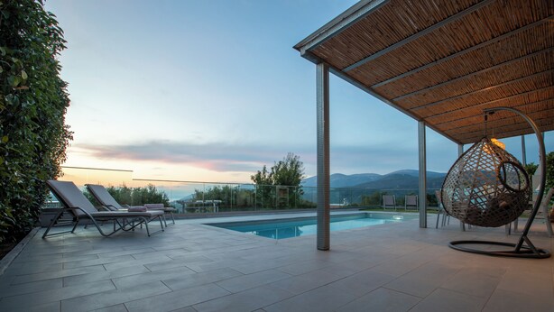 Un área junto a la piscina con sillones de descanso, una hamaca colgante y una pérgola.