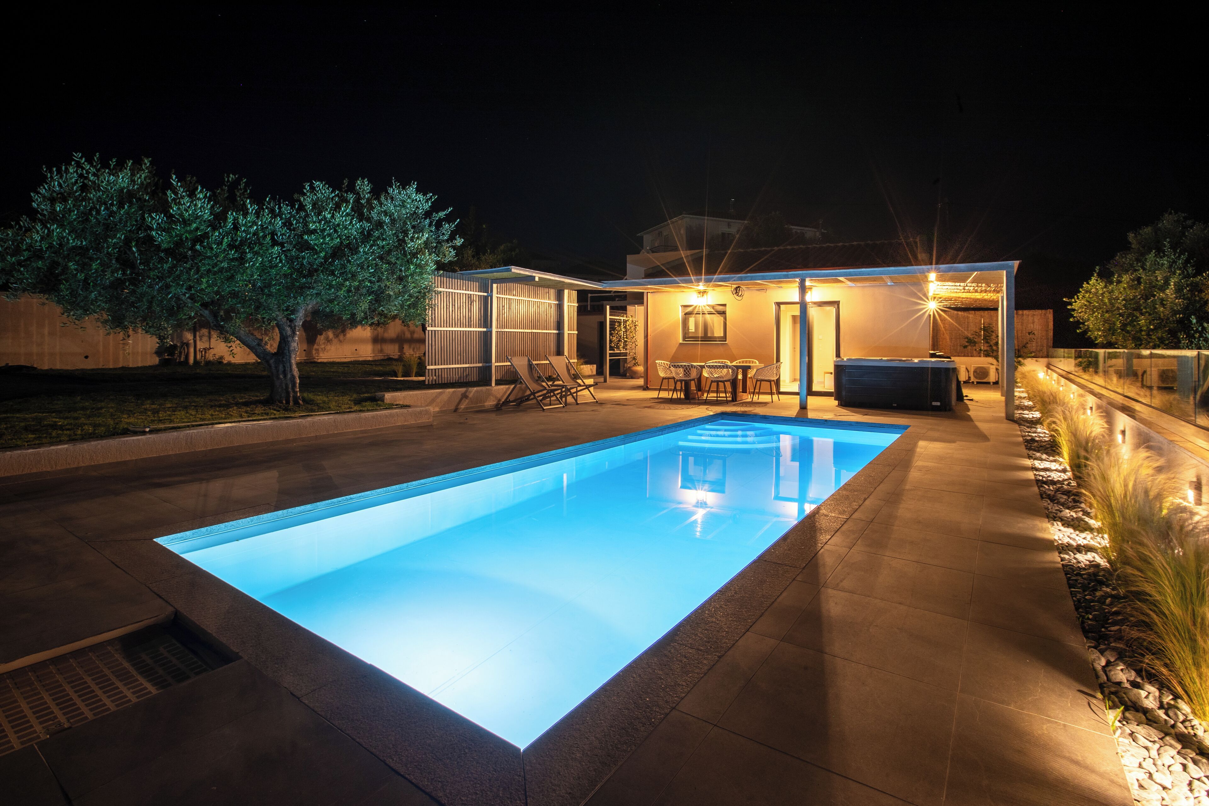 A modern house with a swimming pool, outdoor seating, and a well-lit patio area.