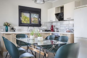 A modern kitchen with a glass dining table, teal chairs, and a window with a black frame.