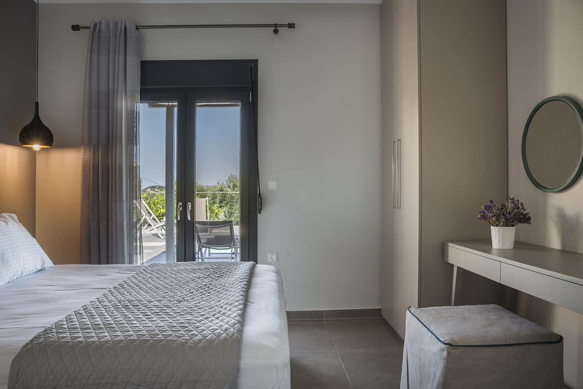 Ein Schlafzimmer mit Bett, Schreibtisch, Stuhl, einer kleinen Hocker, einer Topfpflanze und einem Balkon mit Blick.