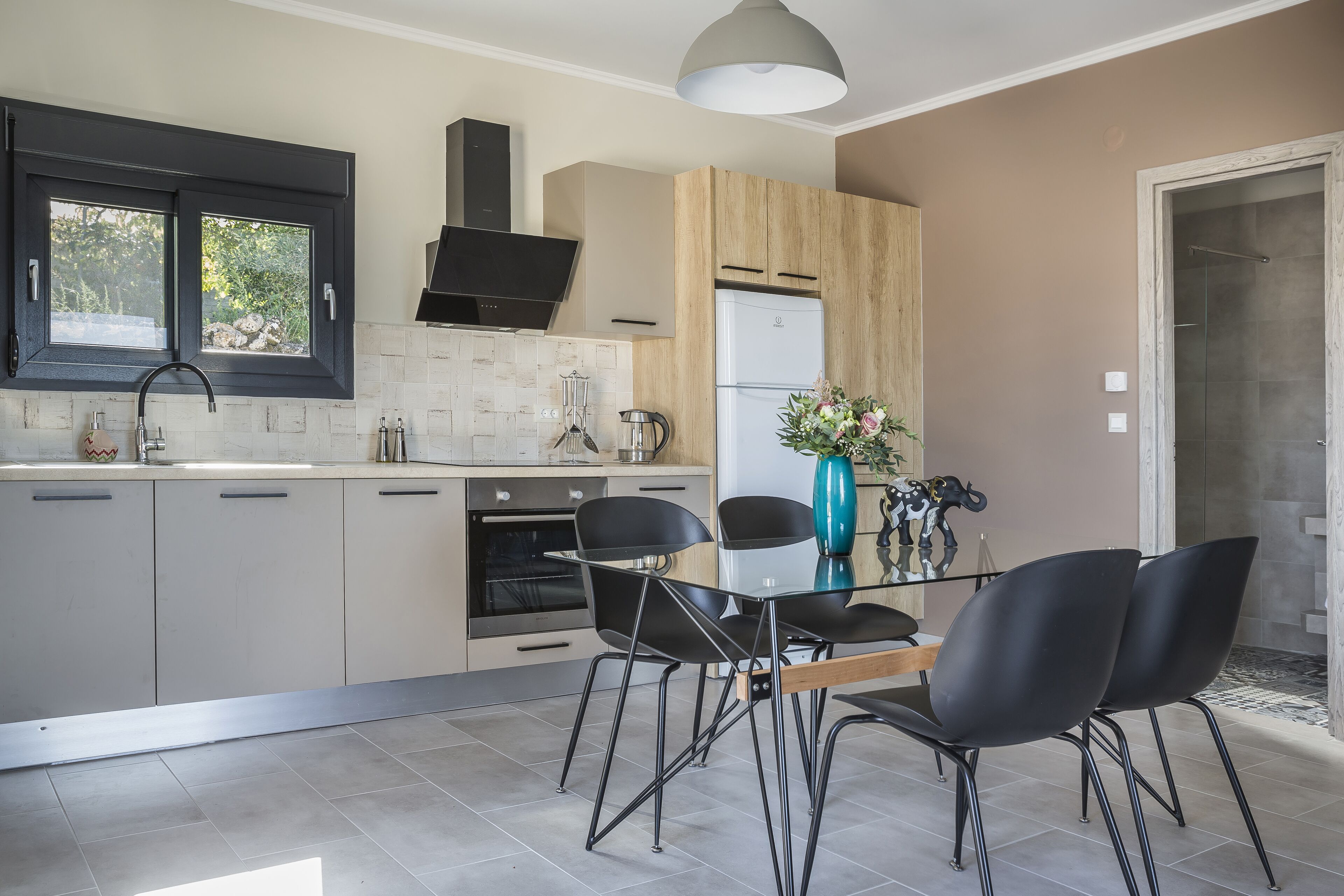 Une cuisine moderne équipée d’un four encastré, d’un réfrigérateur et d’un coin repas avec une table en verre et des chaises noires.