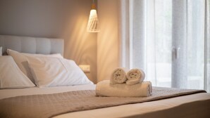 Una cama bien hecha con sábanas blancas y dos toallas enrolladas sobre un edredón color beige.