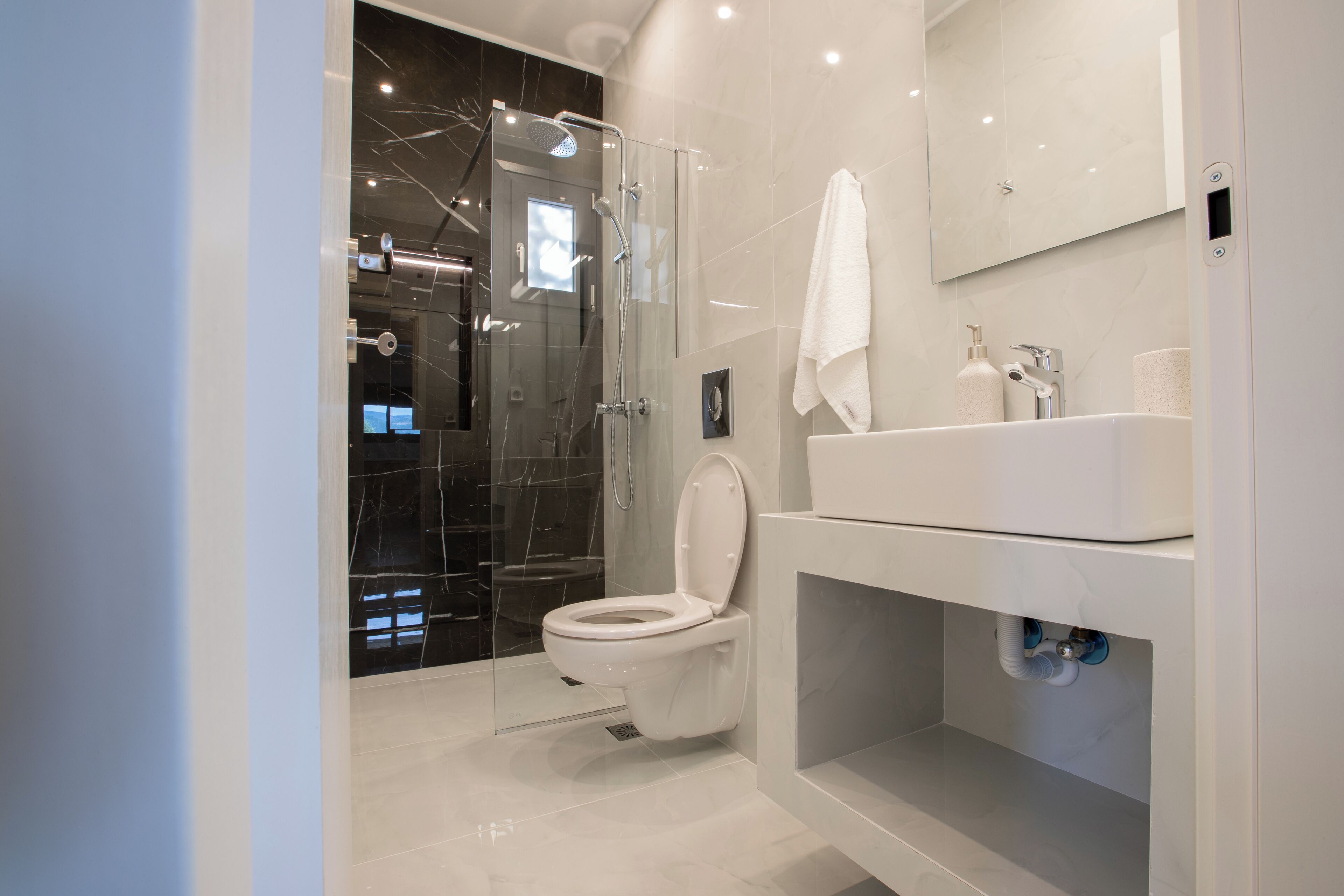 Une salle de bain moderne avec une douche à parois de verre, des toilettes blanches et un lavabo surmonté d’un miroir.