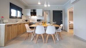 Una cocina moderna con armarios de madera, una mesa de comedor con sillas blancas e iluminación colgante.
