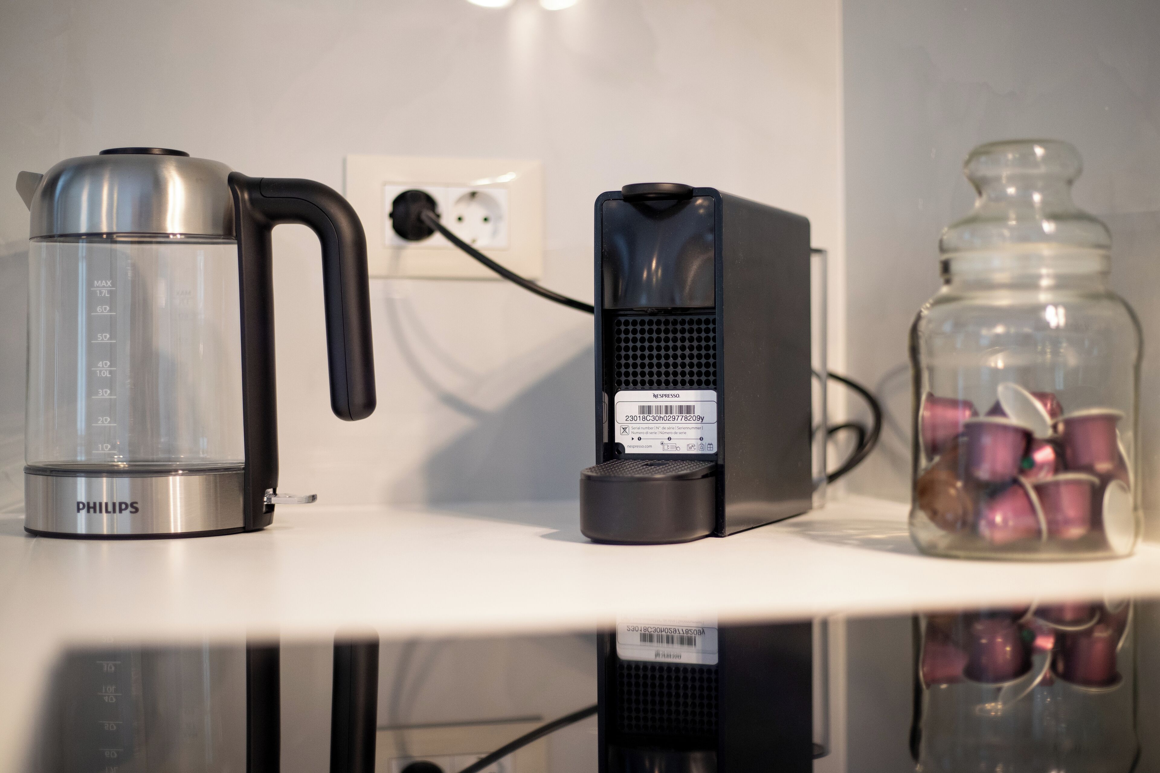 A kitchen counter with a Philips electric kettle, a black coffee maker, and a glass jar with purple mugs.