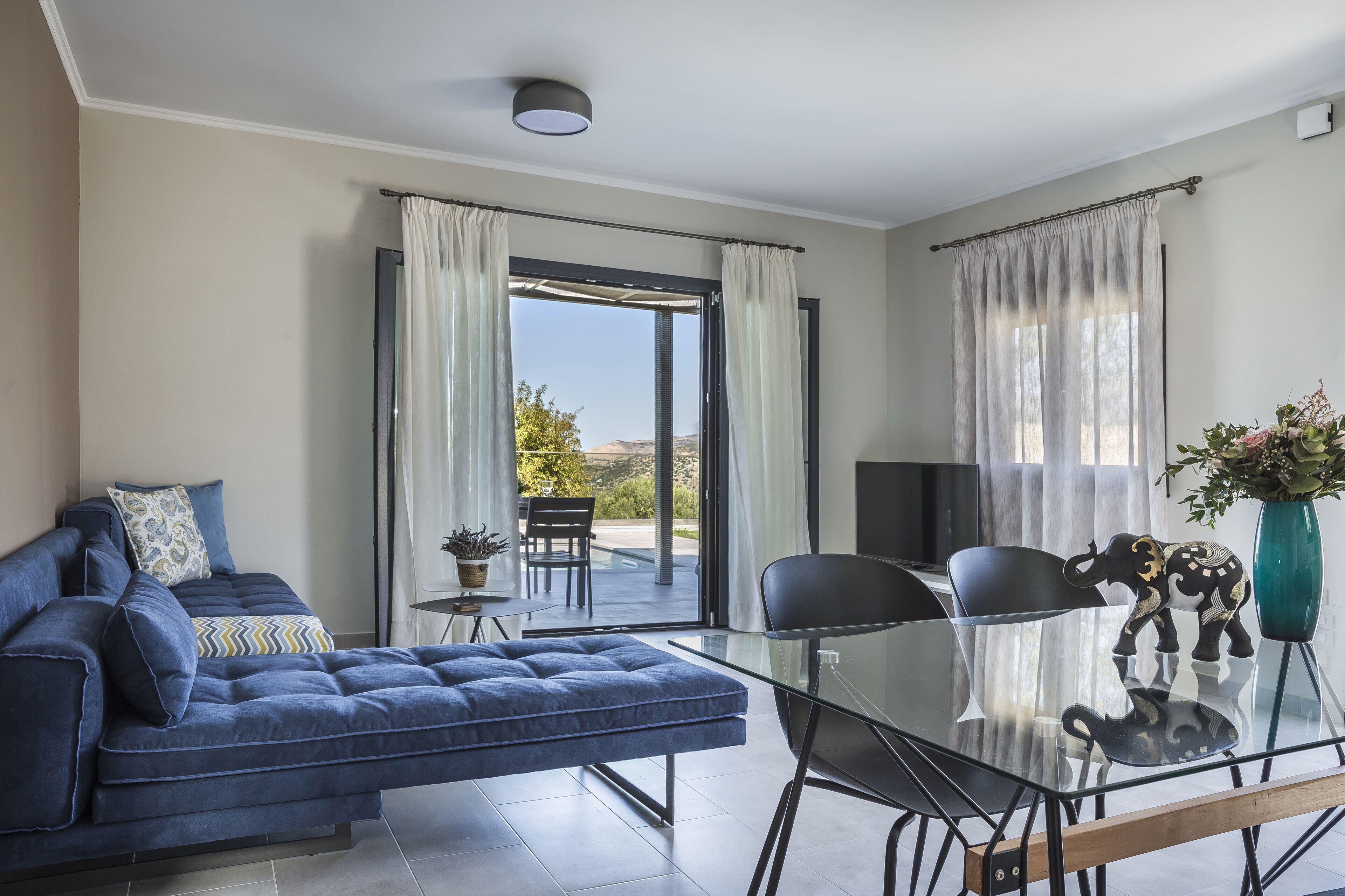 Una sala de estar moderna con un sofá, una mesa de comedor de vidrio y vistas al exterior.