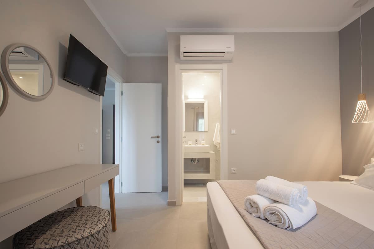 Ein Hotelzimmer mit Bett, Schreibtisch, Fernseher, Klimaanlage und einem sichtbaren Badezimmer hinter einer geöffneten Tür.