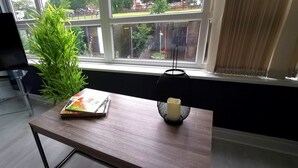 A room with a TV on a glass table, a plant, a book, and a lamp by a window.